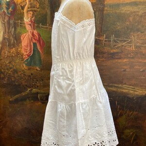 May include: White cotton slip dress with eyelet lace trim. The dress has a gathered waist and a tiered skirt.