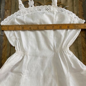 May include: White cotton slip dress with a lace trim and a gathered waist. The dress measures approximately 23 cm across the bust.