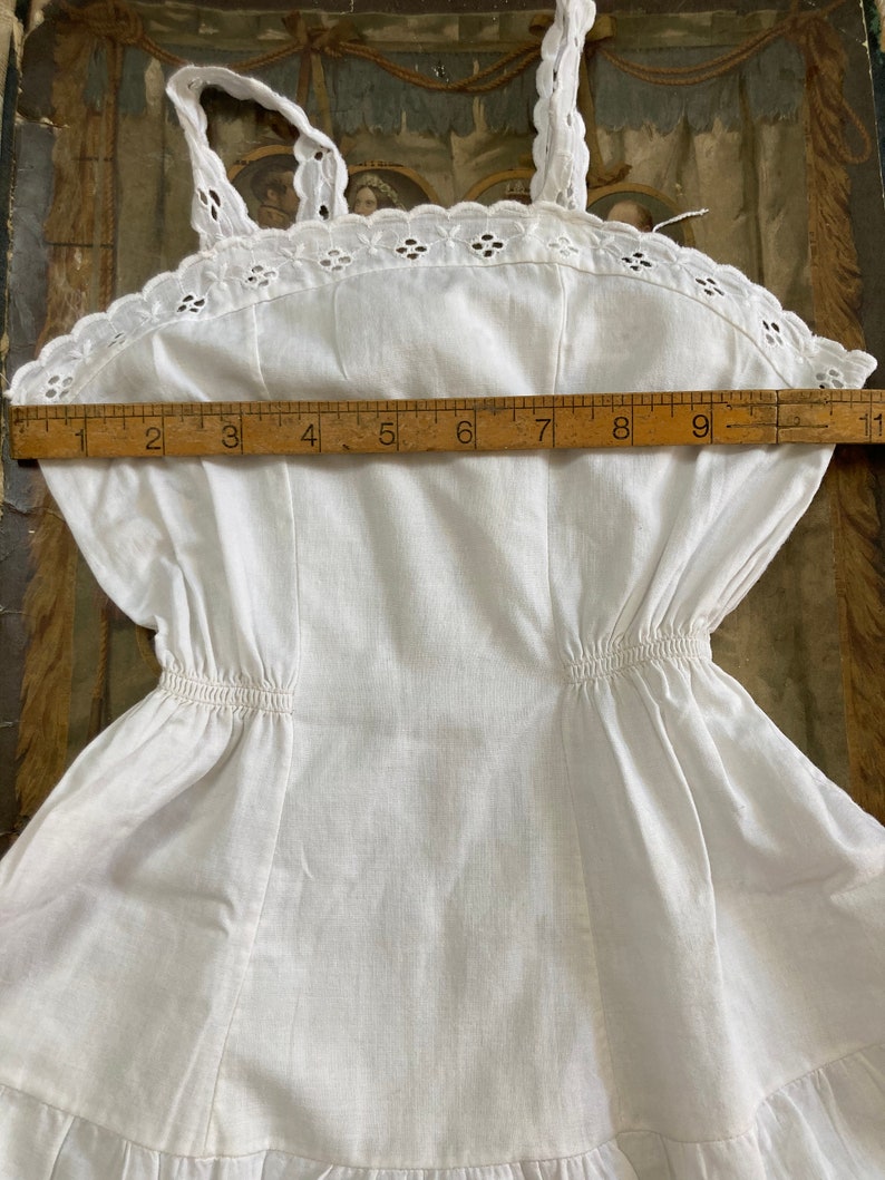 May include: White cotton slip dress with a lace trim and a gathered waist. The dress measures approximately 23 cm across the bust.