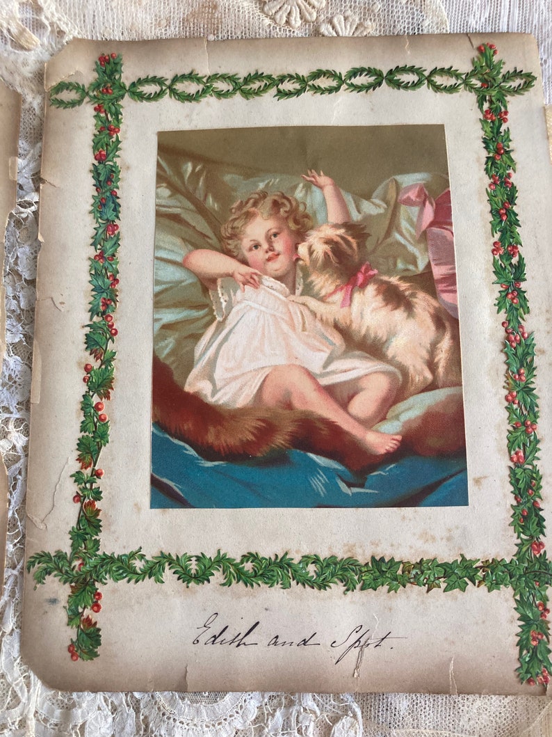May include: An antique Christmas card featuring a young girl in a white dress with a dog. The image is framed with a green holly border and the text "Edith and Spot" is written in cursive at the bottom.