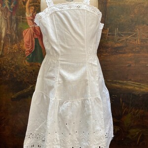 May include: White cotton slip dress with eyelet lace trim and a tiered skirt. The dress is on a mannequin and has a vintage look.
