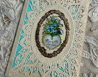 Puede incluir: Una tarjeta de encaje vintage con un ramo de flores azules de nomeolvides en un marco en forma de corazón. La tarjeta tiene un borde dorado y el texto "Forget me not".
