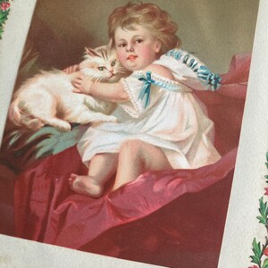 May include: A vintage illustration of a young girl in a white dress holding a white cat. The girl is sitting on a red velvet cushion and the cat is resting on her lap. The illustration is framed with a green floral border.