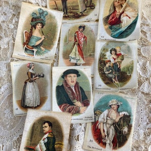 May include: A collection of vintage cigarette cards featuring various illustrations, including a woman with a blue hat, a man in a fur coat, a woman with a milk pail, and a woman with a child. The cards are printed on white paper with colourful illustrations and text.
