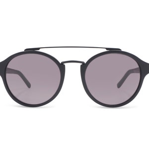 Puede incluir: Gafas de sol redondas negras con un puente metálico fino y lentes grises oscuras.