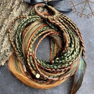 Può includere: Un set di extensioni per capelli intrecciati in tonalità di marrone, verde e biondo. Le extensioni sono legate insieme con un nastro nero e un elastico marrone. Ci sono perline di legno e un accento di piuma.
