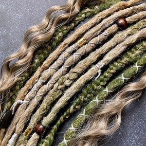 Puede incluir: Primer plano de un conjunto de rastas sintéticas en tonos verdes y beige. Las rastas están atadas con cuerda blanca y decoradas con cuentas de madera y oro.