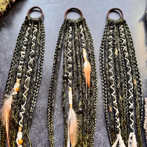 Könnte beinhalten: Drei grüne und schwarze Haarverlängerungen mit Perlen, Federn und Schnurakzente. Die Verlängerungen sind mit braunen Gummibändern zusammengebunden.