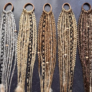 Può includere: Sei set di extensioni per capelli sintetici con perline di legno, ogni set è legato con un elastico marrone. Le extensioni per capelli sono in varie tonalità di marrone, biondo e grigio.