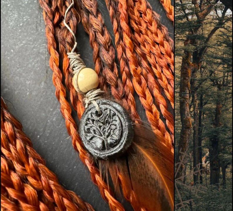 May include: Close-up of a set of braided hair extensions in a reddish-brown color. The extensions are adorned with a small wooden bead and a charm featuring a tree design. The charm is attached to a brown feather.