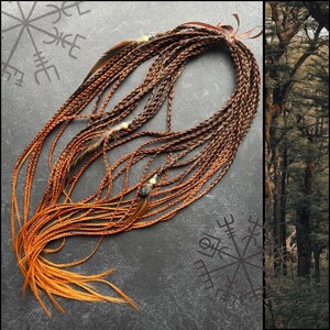 May include: A long, thick braid of brown and orange hair with feathers and beads. The braid is on a dark gray surface with a compass symbol.