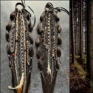 Puede incluir: Dos juegos de extensiones de cabello marrón con cuentas y dijes. Las extensiones están atadas juntas con una banda elástica marrón. Las extensiones cuelgan sobre un fondo gris.