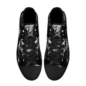 May include: A pair of black high-top canvas shoes with a white and gray abstract design. The shoes have black laces and a white rubber sole.