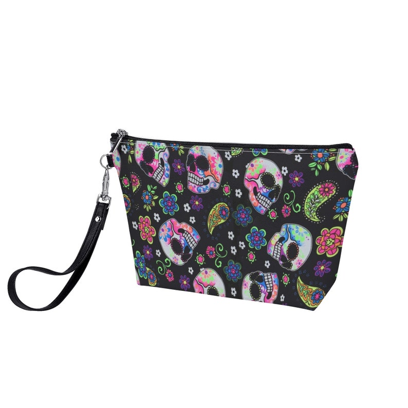 May include: Black zippered makeup bag with a colorful skull and floral pattern. The bag has a black strap.