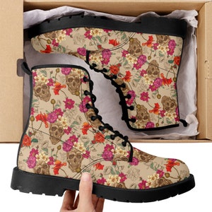 Może przedstawiać: Para czarnych sznurowanych butów z kwiatowym i czaszkowym nadrukiem. Buty mają beżowe tło z różowymi, czerwonymi i białymi kwiatami oraz brązowymi czaszkami.