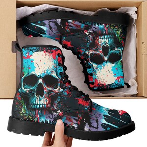 Może przedstawiać: Czarne skórzane buty z kolorowym wzorem czaszki i rozpryskującej się farby. Buty mają sznurowadła i grubą podeszwę.