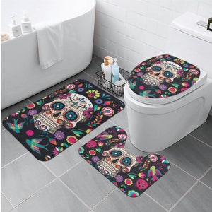 Puede incluir: Un juego de tres alfombras de ba&ntilde;o con un dise&ntilde;o de calavera de az&uacute;car colorido con detalles florales. El juego incluye una tapa para el asiento del inodoro, una alfombra de contorno y una alfombra rectangular m&aacute;s grande.