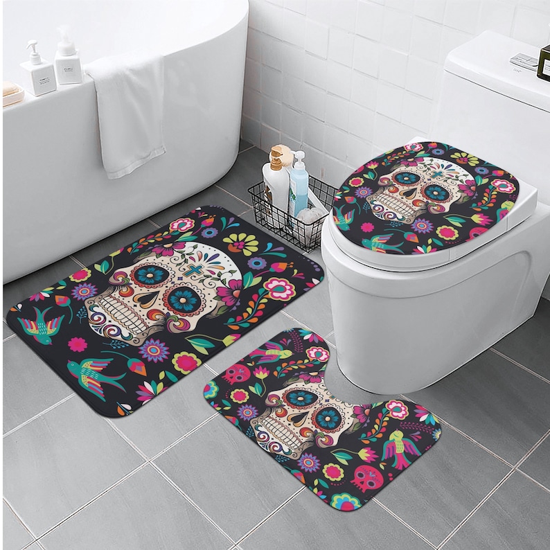 Puede incluir: Un juego de tres alfombras de ba&ntilde;o con un dise&ntilde;o de calavera de az&uacute;car colorido con detalles florales. El juego incluye una tapa para el asiento del inodoro, una alfombra de contorno y una alfombra rectangular m&aacute;s grande.