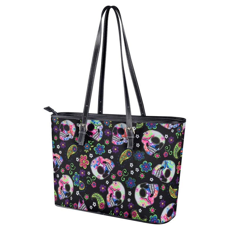 May include: Black leather tote bag with a colorful sugar skull pattern. The skulls are decorated with flowers and paisley designs.