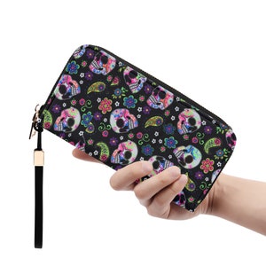 May include: A black zippered wallet with a colorful skull and floral pattern. The wallet has a wrist strap.