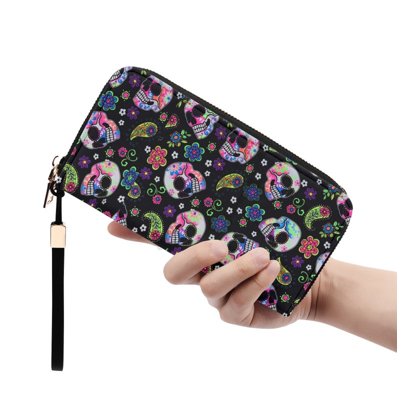 May include: A black zippered wallet with a colorful skull and floral pattern. The wallet has a wrist strap.
