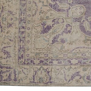 K&ouml;nnte beinhalten: Nahaufnahme eines Vintage-Teppichs mit beigefarbenem Hintergrund und violetter Umrandung. Der Teppich hat ein florales Muster mit filigranen Details.