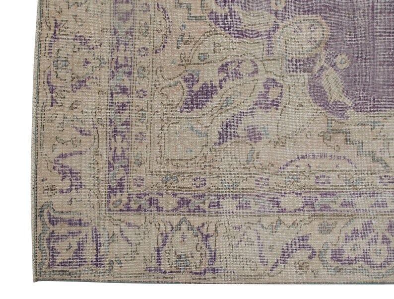 K&ouml;nnte beinhalten: Nahaufnahme eines Vintage-Teppichs mit beigefarbenem Hintergrund und violetter Umrandung. Der Teppich hat ein florales Muster mit filigranen Details.