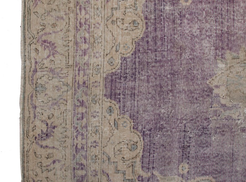 K&ouml;nnte beinhalten: Ein Vintage-Teppich mit einem violetten Mittelteil und einem beigefarbenen Rand. Der Rand hat ein Blumenmuster.