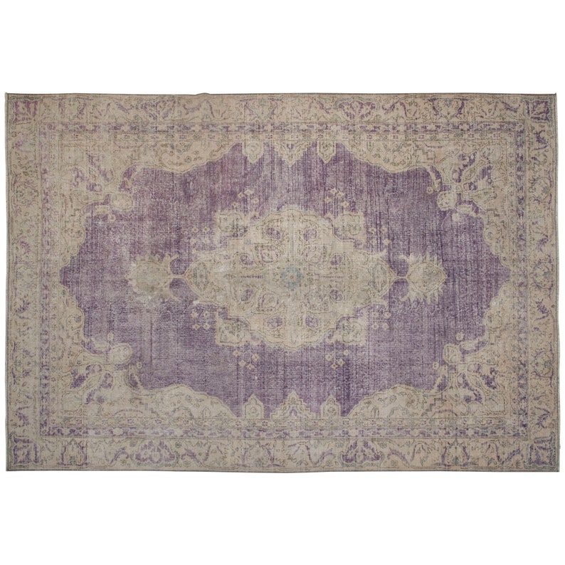 K&ouml;nnte beinhalten: Ein Vintage-Teppich mit einem violetten Hintergrund und einem beigefarbenen Muster. Der Teppich hat einen verblassten, abgenutzten Look und zeigt komplizierte florale Designs.