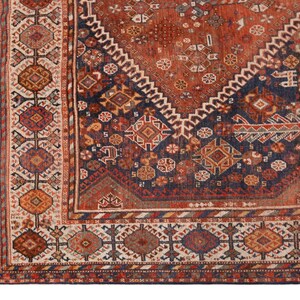 May include: Close-up of a section of an antique rug with a detailed geometric pattern. The rug features a rich color palette of rust, navy blue, cream, and touches of gold. The design includes diamond shapes, floral motifs, and intricate borders.
