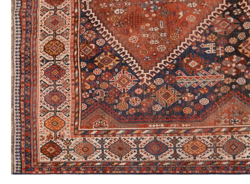 May include: Close-up of a section of an antique rug with a detailed geometric pattern. The rug features a rich color palette of rust, navy blue, cream, and touches of gold. The design includes diamond shapes, floral motifs, and intricate borders.