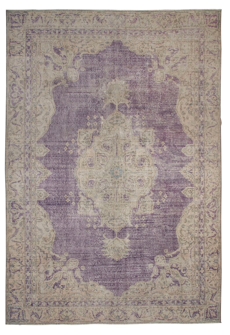 K&ouml;nnte beinhalten: Ein Vintage-Teppich mit einem violetten Hintergrund und einem beigefarbenen Muster. Der Teppich hat ein zentrales Medaillon mit komplizierten Details und einen Rand mit floralen Motiven.