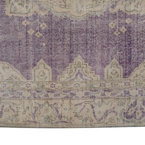 K&ouml;nnte beinhalten: Ein Vintage-Teppich mit einem violetten Hintergrund und einem beigefarbenen Rand. Der Rand zeigt ein florales Muster mit komplizierten Details.