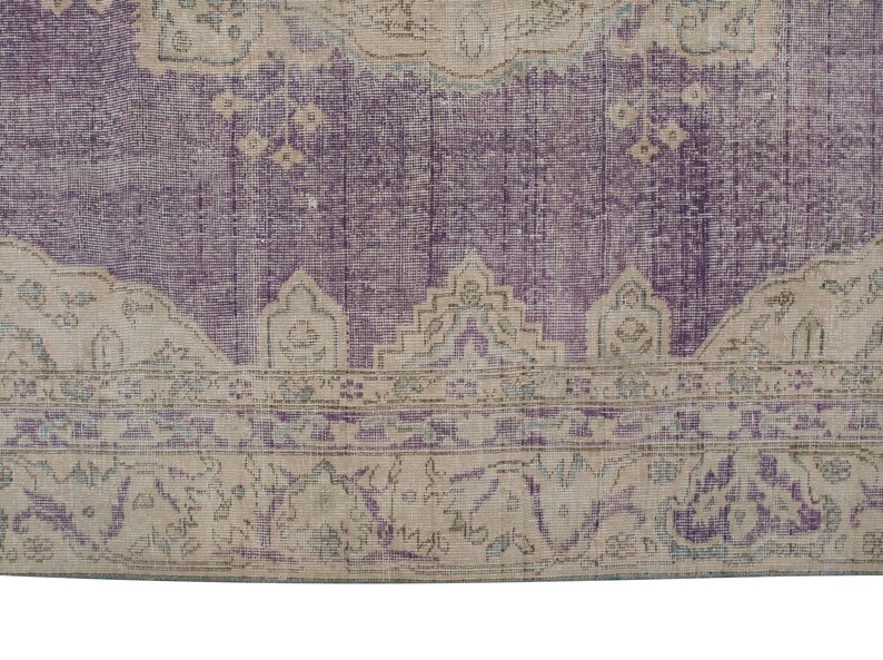 K&ouml;nnte beinhalten: Ein Vintage-Teppich mit einem violetten Hintergrund und einem beigefarbenen Rand. Der Rand zeigt ein florales Muster mit komplizierten Details.