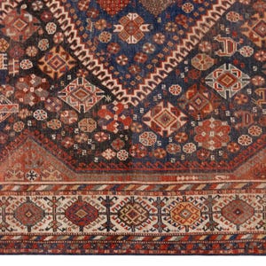 May include: Close-up of a section of an antique rug with a complex geometric pattern. The rug features a deep navy blue field with red, brown, and cream-colored geometric shapes. The border has a repeating pattern of diamonds and other shapes.