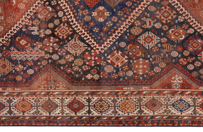 May include: Close-up of a section of an antique rug with a complex geometric pattern. The rug features a deep navy blue field with red, brown, and cream-colored geometric shapes. The border has a repeating pattern of diamonds and other shapes.
