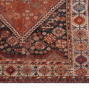 May include: Close-up of a section of an antique rug with a geometric pattern. The rug features a central diamond design in shades of red and navy blue, with intricate borders in cream, red, and blue. The rug's design is detailed and complex.