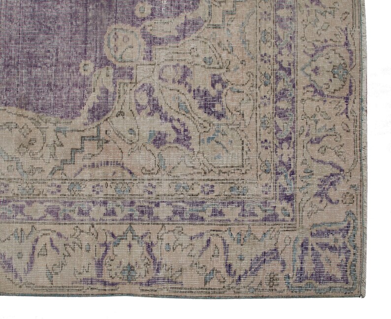 K&ouml;nnte beinhalten: Ein Vintage-Teppich mit einem verblassten Farbverlauf in Lila und Beige. Der Teppich hat ein florales Muster mit filigranen Details. Der Teppich ist in gutem Zustand und hat eine weiche Textur.