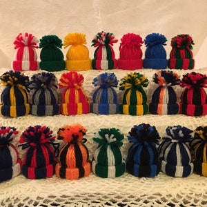 May include: A collection of 24 colorful knitted hats with pom-poms. The hats are arranged in three rows of eight, with each row featuring a different color combination.