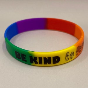 May include: A rainbow coloured silicone bracelet with the text "BE KIND" in black lettering and two hand signs in American Sign Language for "kind".