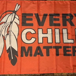 May include: A red flag with the text "EVERY CHILD MATTERS" in black letters and a white feather design.