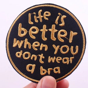 May include: A round black patch with gold embroidered text that reads "life is better when you don't wear a bra".