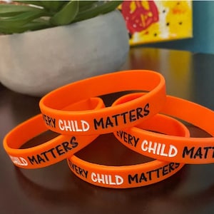 May include: Four orange silicone wristbands with the text "Every Child Matters" printed in black.