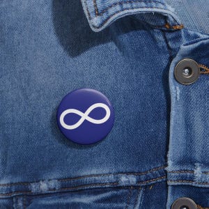 May include: A blue button with a white infinity symbol. The button is pinned to a denim jacket.
