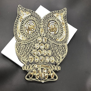 May include: A gold and black sequined owl applique. The owl is detailed with intricate embroidery and sequins.