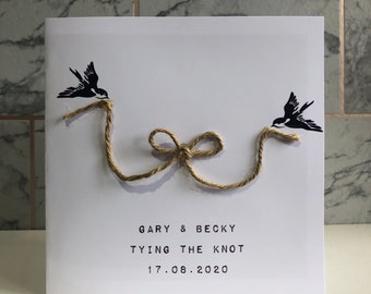 May include: White wedding card with black bird silhouettes and a twine bow. The text reads "GARY & BECKY TYING THE KNOT 17.08.2020". A simple and elegant design for a wedding or engagement.