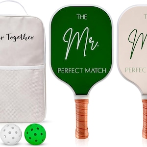 Op de afbeelding: Een set van twee pickleball-peddels, één donkergroen en één crème, met bruine, getextureerde handvatten. De groene peddel heeft de tekst THE Mr. PERFECT MATCH en de crème peddel THE Mrs. PERFECT MATCH. Inclusief een crème rugzak met de tekst Better Together en twee ballen.