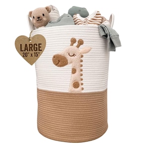 May include: A large, round, woven rope basket with a giraffe applique. The basket is two-toned, with a tan bottom and white top. The tag reads "LARGE 20" x 15"". The basket is filled with baby clothes and a teddy bear.