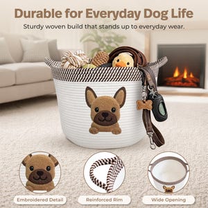 Op de afbeelding: Witte geweven hondenmanden met een bruin en zwart gestreepte rand en een bruin geborduurd honden gezicht. De mand bevat hondenspeelgoed, een riem en een afvalzak dispenser. Tekst op de afbeelding luidt "Durable for Everyday Dog Life".