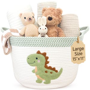 May include: A white and sage green woven rope basket featuring a green dinosaur applique. The basket contains a beige knit bear, a brown plush bear, a small white crochet rabbit, and folded muslin cloths. A tag reads Large Size 15"x11".
